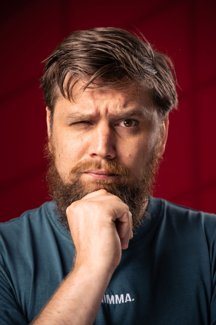 Ik kijk een beetje fronsend, maar recht in de camera. Mijn gezicht leunt deels op mijn vuist.