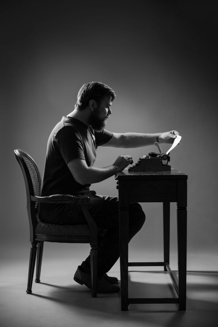 Ik ben stilistisch vanaf opzij gefotografeerd terwijl ik aan een klassiek houten tafel zit. Hel beeld is zwartwit.